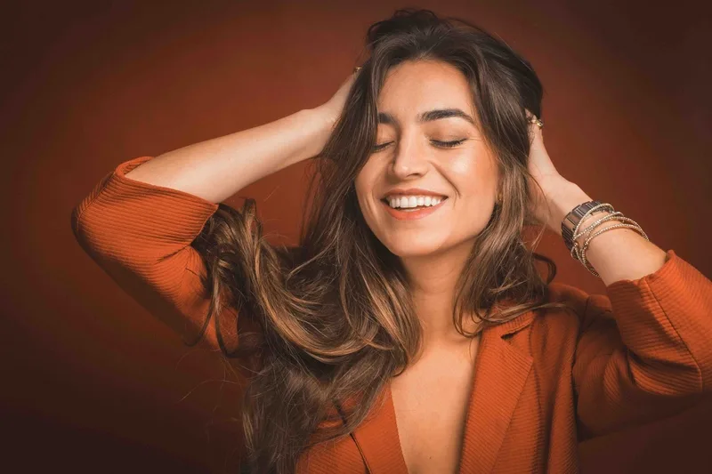 A smiling woman with her hands resting in her hair